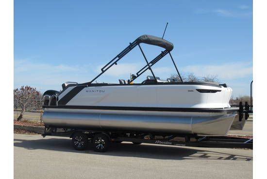 Pontoon boat on trailer, silver and white with black canopy, parked outside on a sunny day.