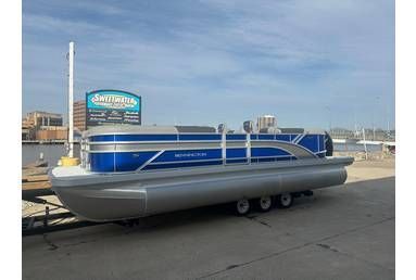 Blue and silver pontoon boat on trailer, near water with sign.