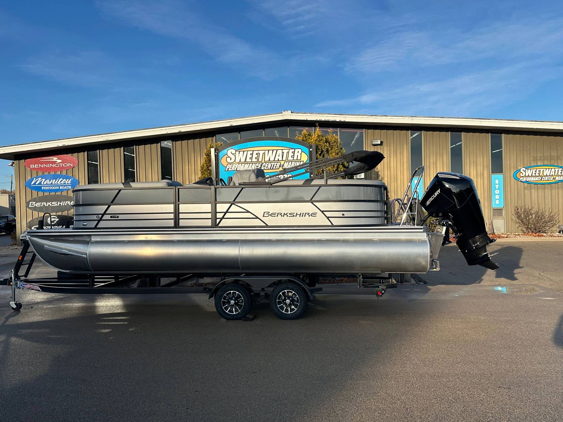 Pontoon boat on trailer in front of a building with blue sky.