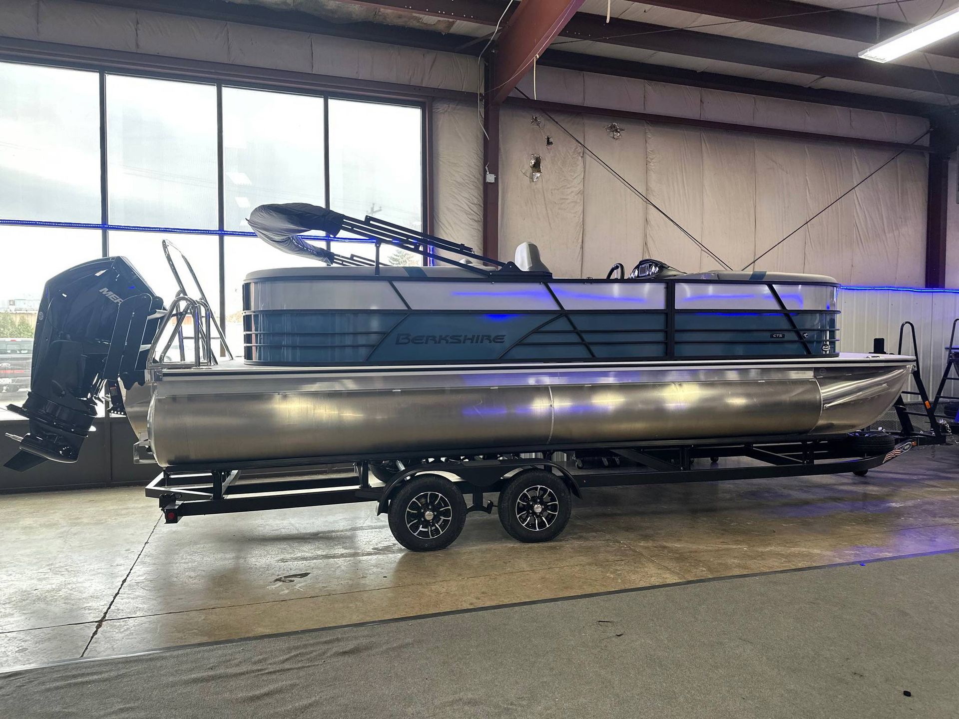 Pontoon boat on trailer in a building, with large windows.