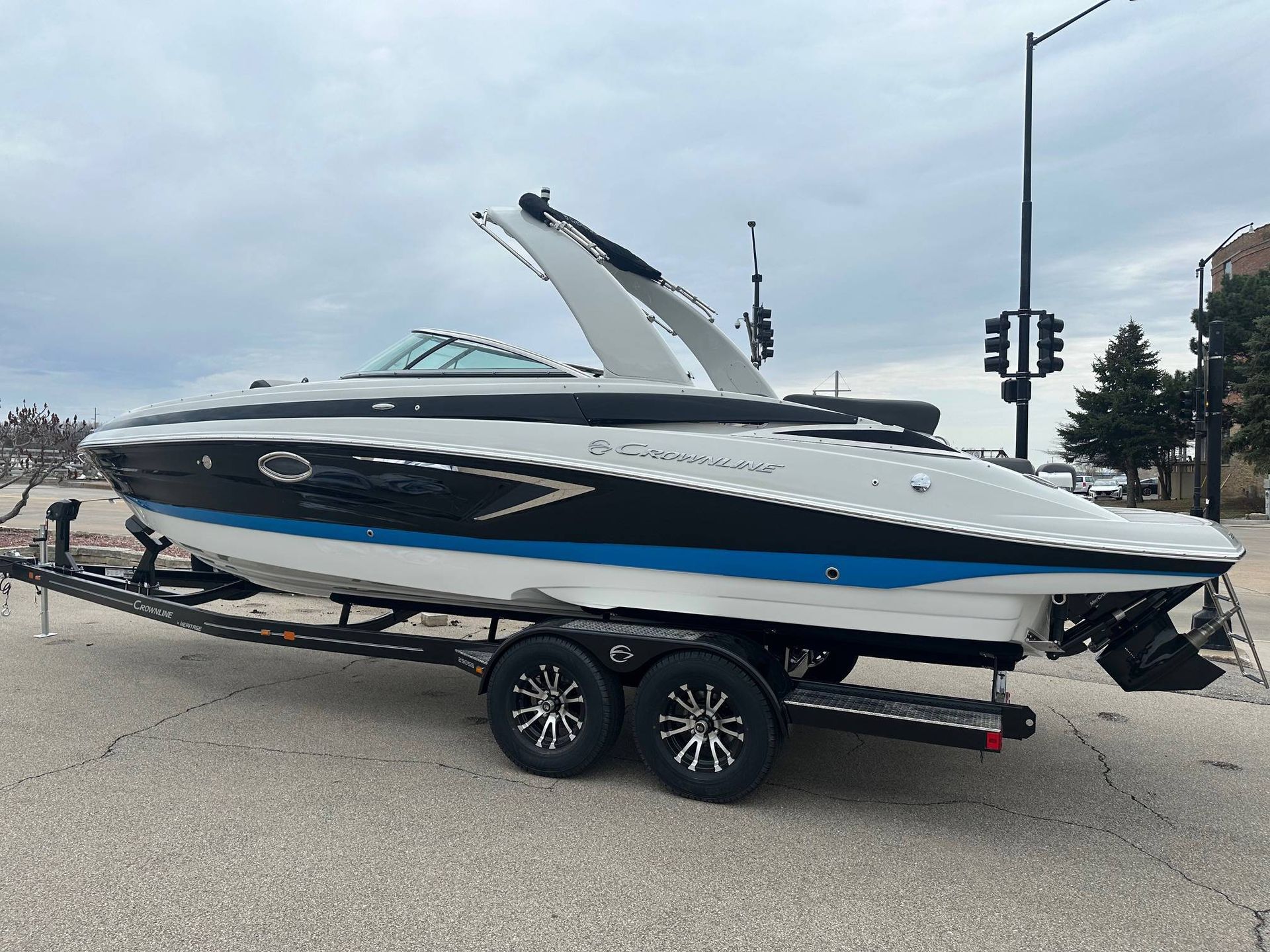 Boat on a trailer, white and black hull with blue stripe, parked on a street.