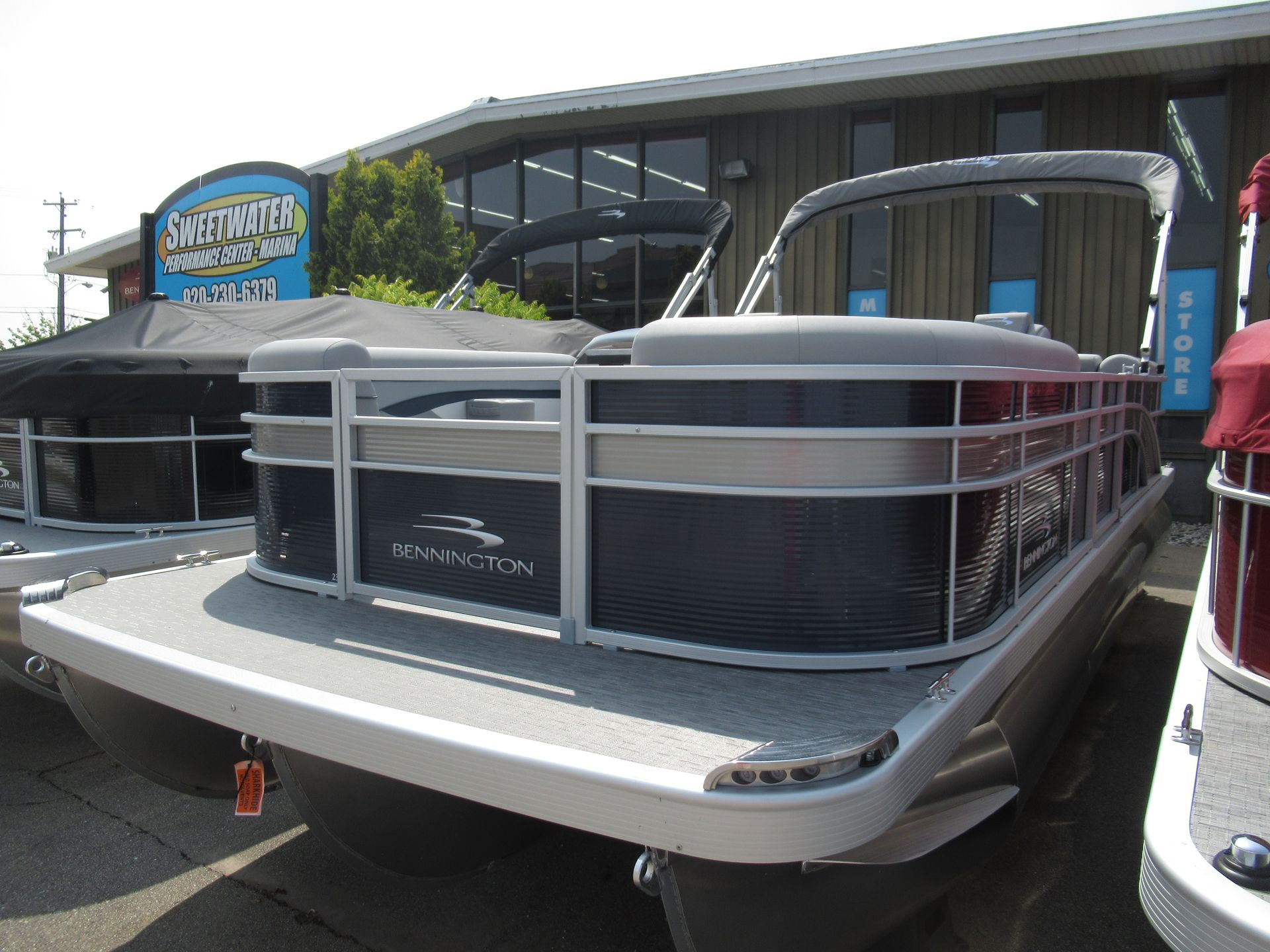Pontoon boat with silver railings and a gray deck, parked outside a store.