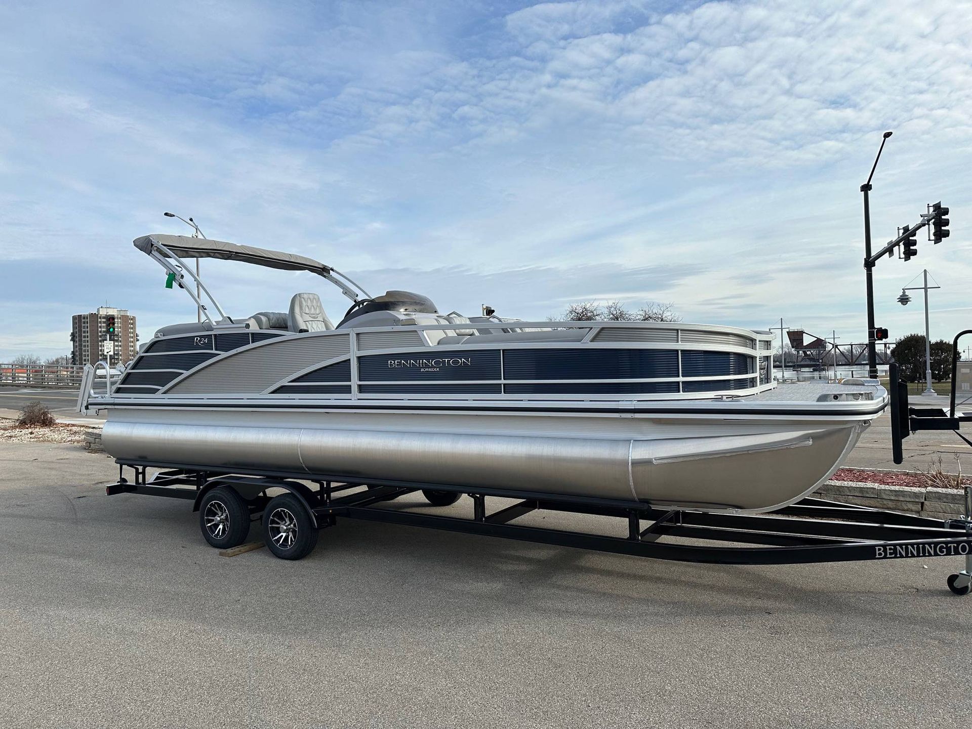 Pontoon boat on trailer, silver and black, with a blue sky background.