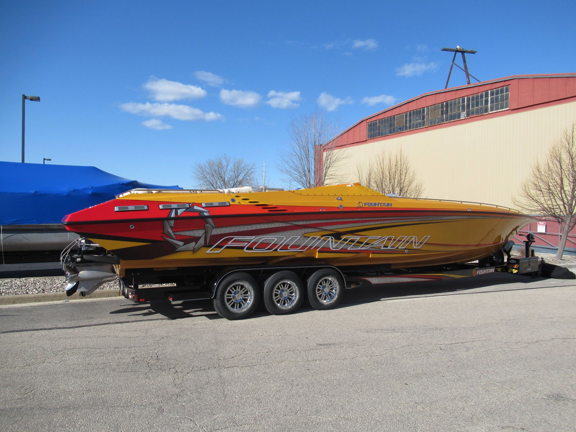 Yellow and red speed boat on a trailer, with silver accents, against a building and blue sky.