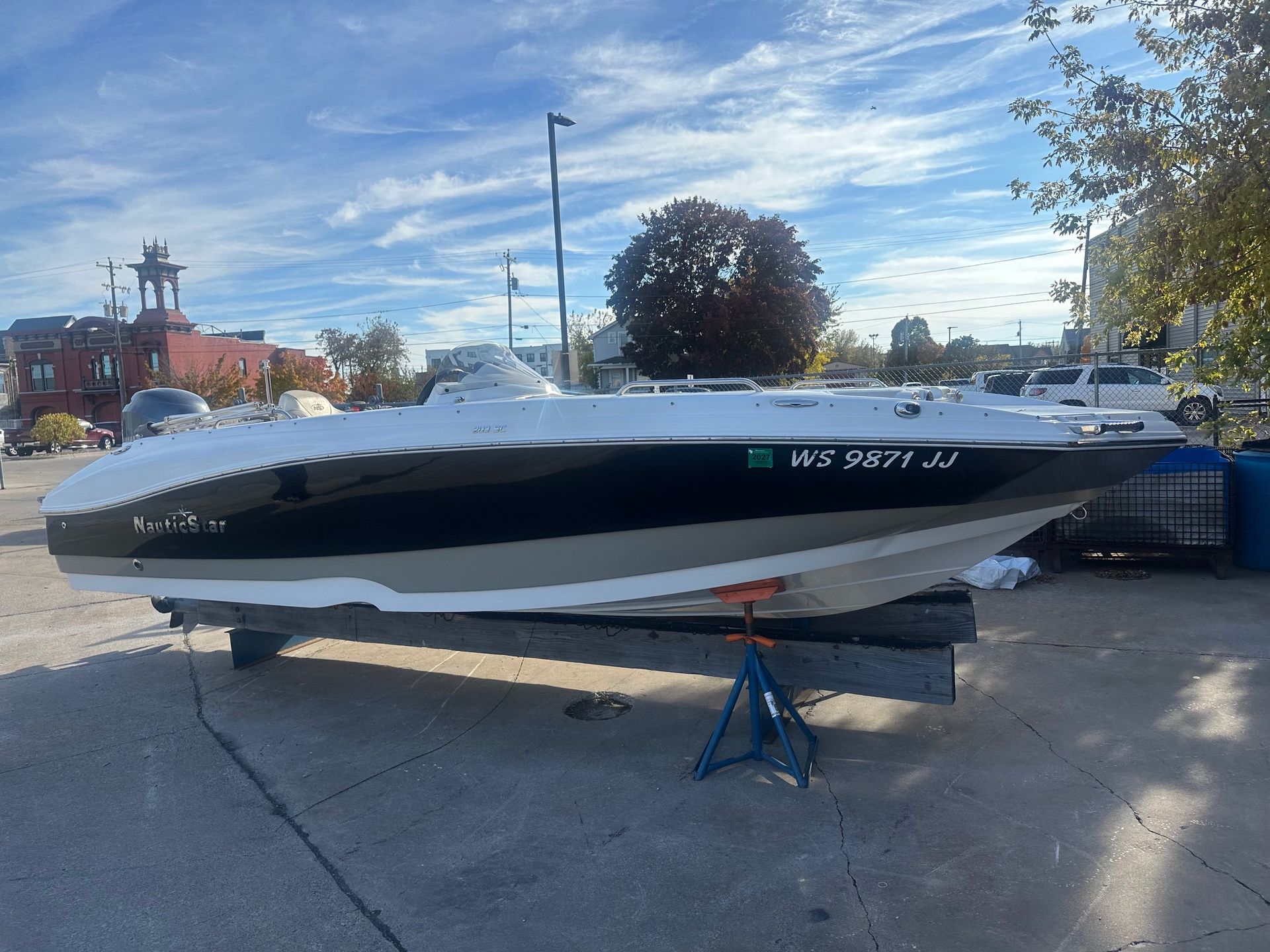 Boat on a concrete pad with blue sky background. White and black boat resting on stands.