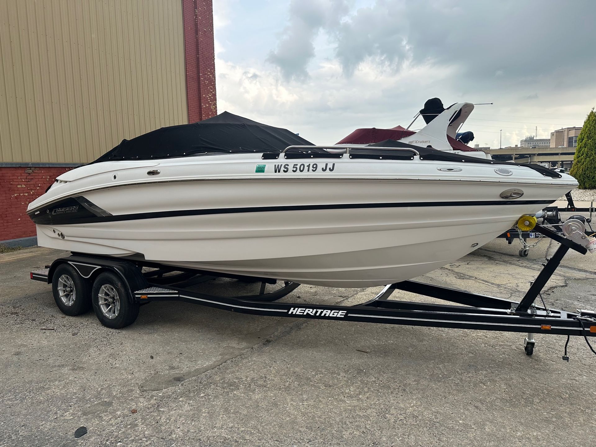 White speedboat on a trailer, with a black cover, parked on concrete.