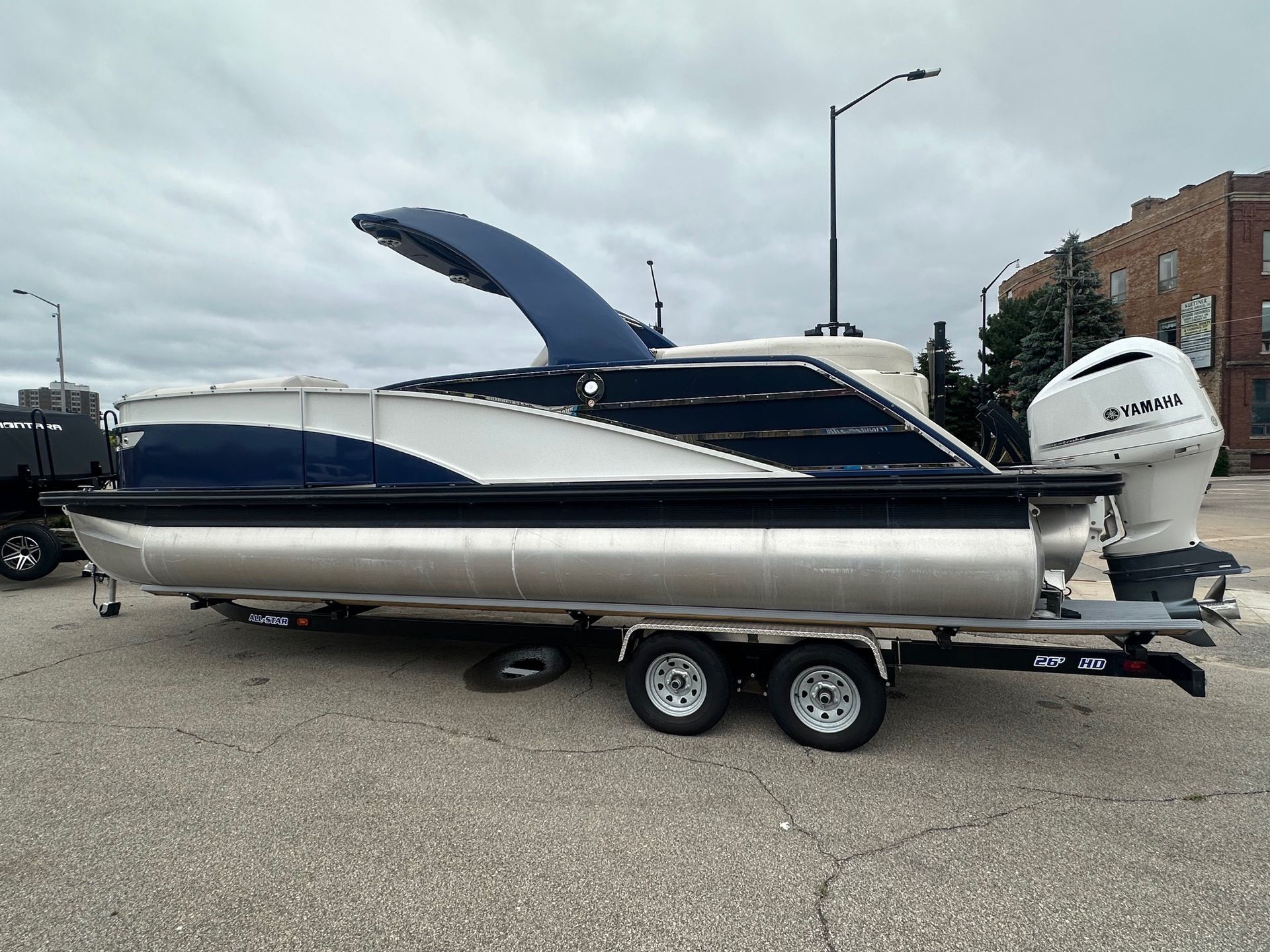 Blue and white pontoon boat on a trailer, with a white outboard motor, parked on pavement.