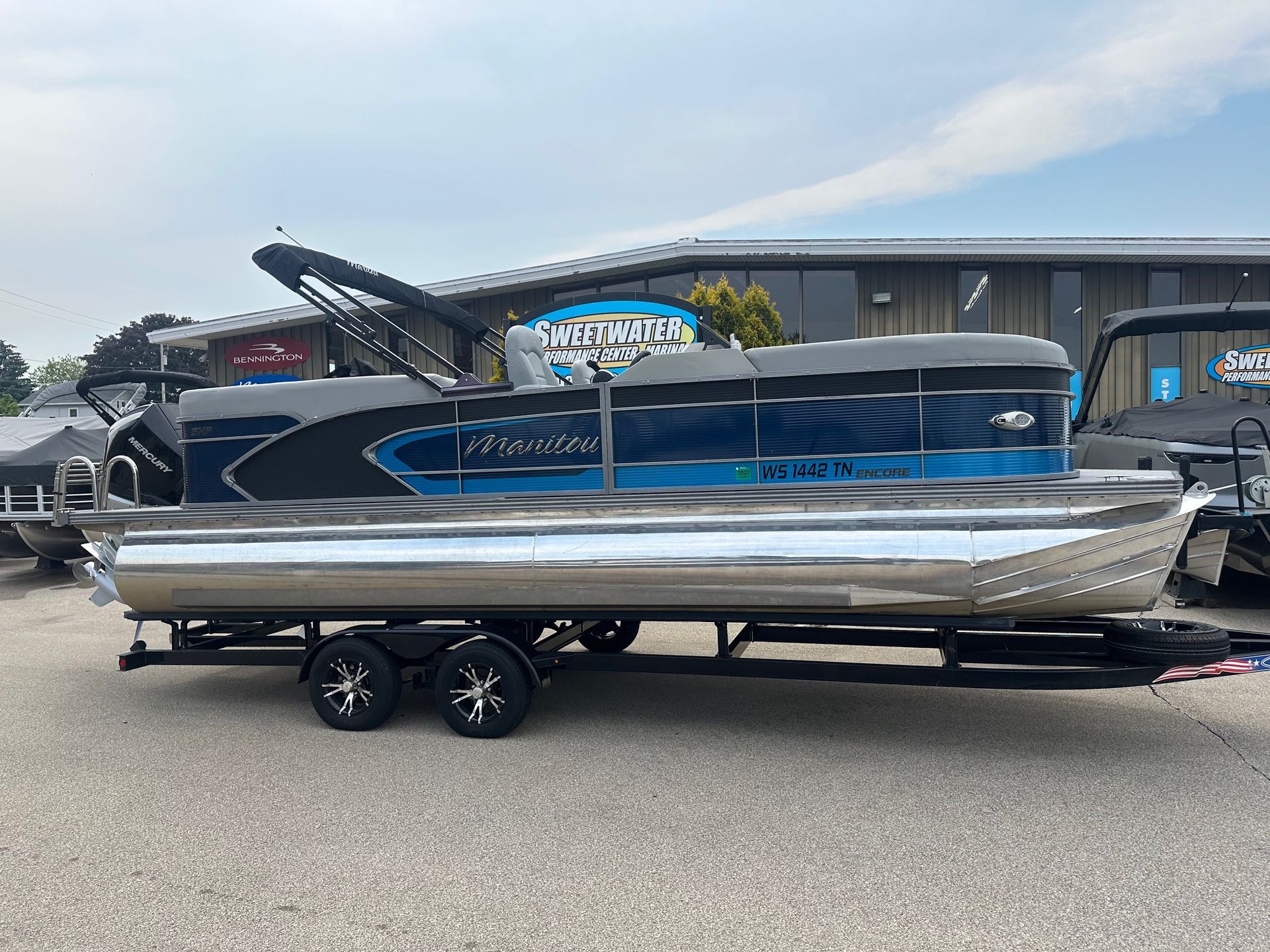 Pontoon boat on trailer, blue and silver, parked outside a building.