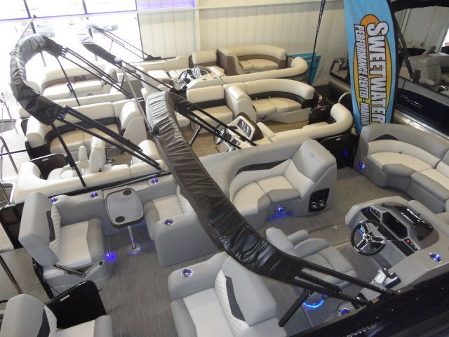 Overhead view of several pontoon boats with gray and white seating, some with black overhead supports, indoors.