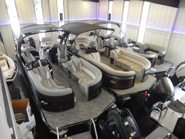 Pontoon boats displayed in a showroom. Black and silver hulls, tan and gray seating.
