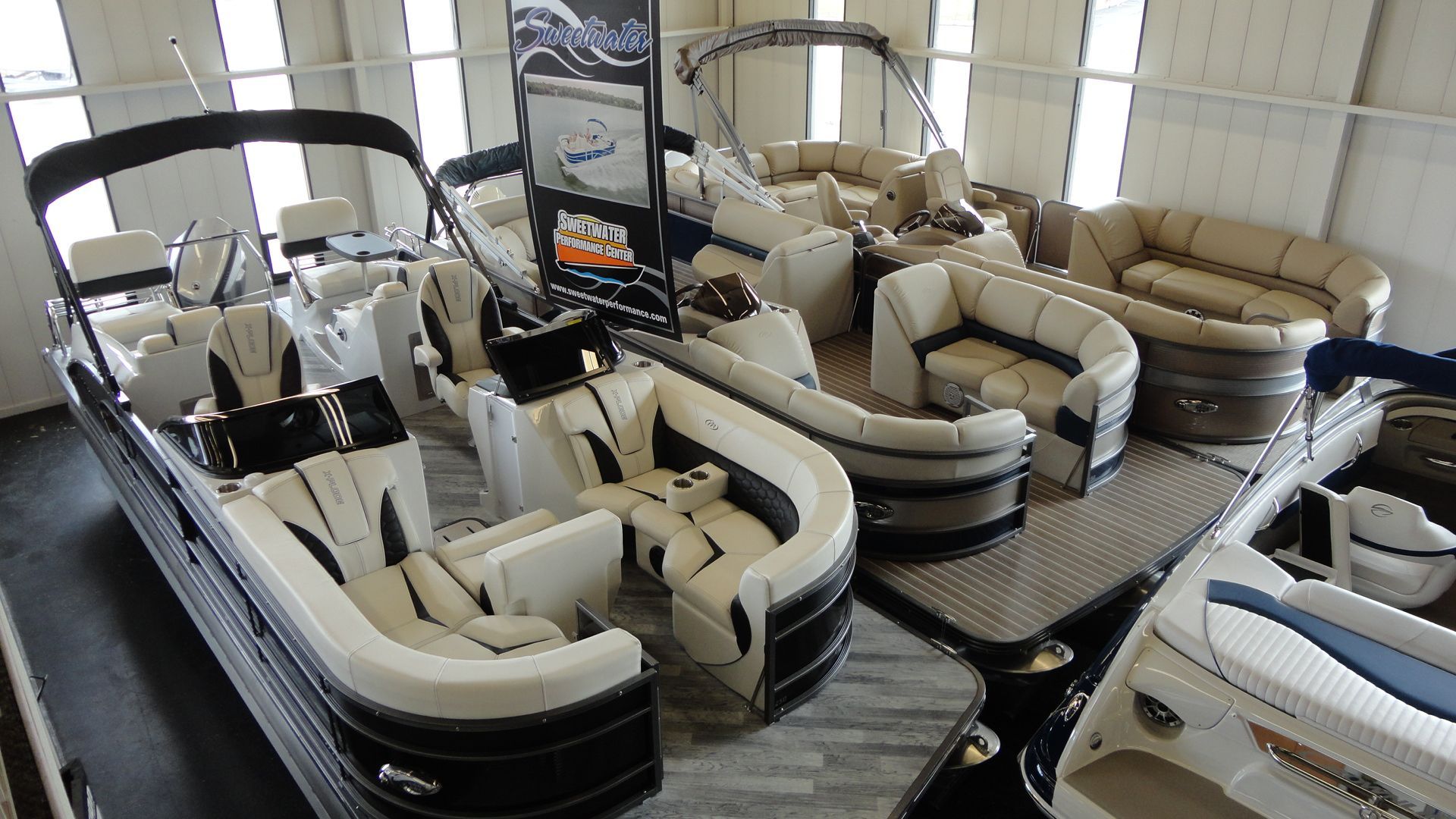 Boats on display in a showroom, white and tan upholstery, open seating.
