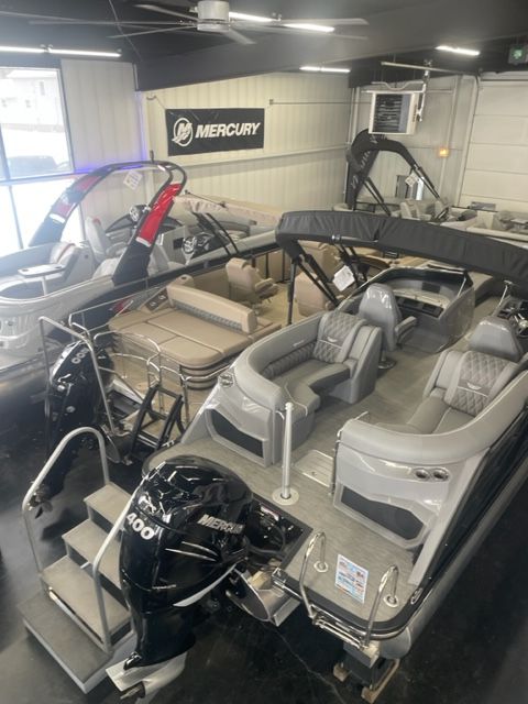 Two pontoon boats inside a showroom, one with a Mercury engine.