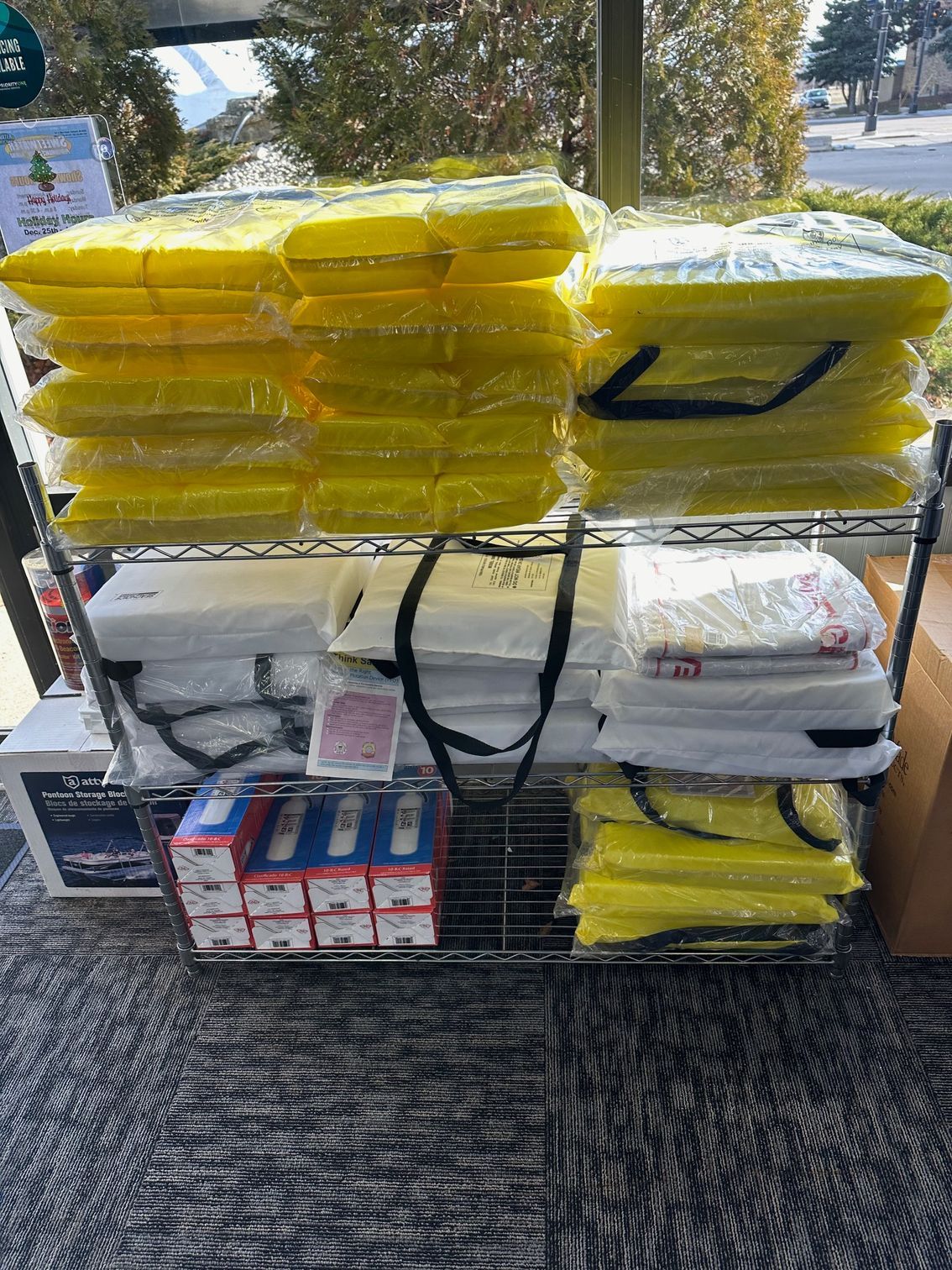 Metal shelving unit holding stacked yellow and white packages, assorted boxes, and a black handled bag.