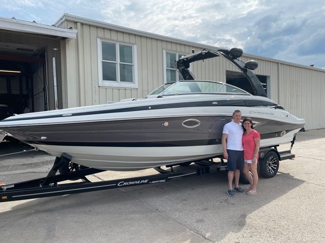 Couple standing beside a white and brown boat on a trailer, in front of a building.
