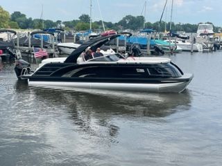 Black and silver pontoon boat on water with people aboard near a marina.