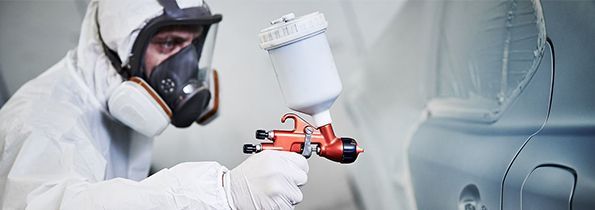 A man in a protective suit is spray painting a car.