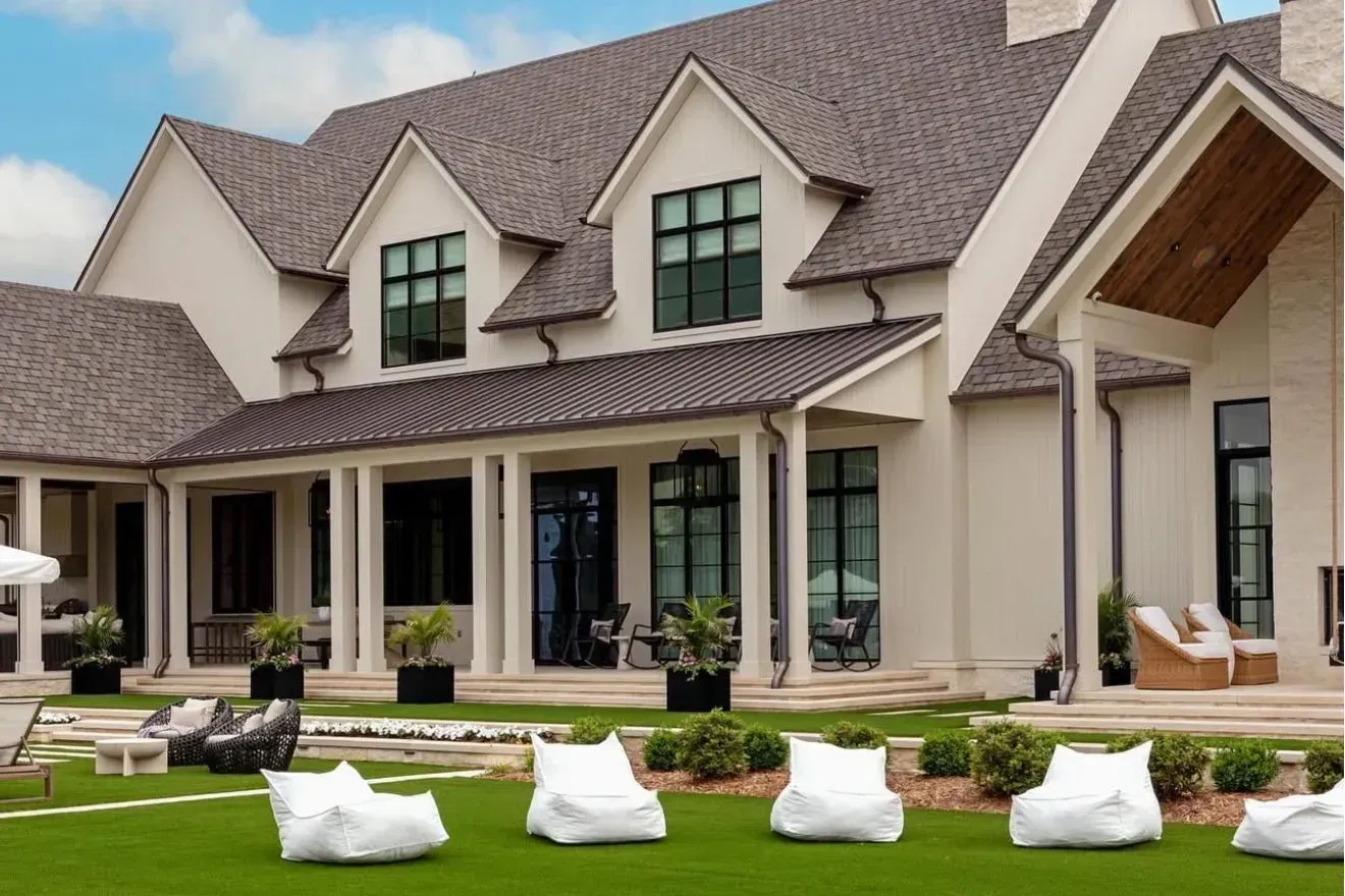 A multi-story beige house with a dark gabled roof and a spacious lawn featuring white beanbag chairs.