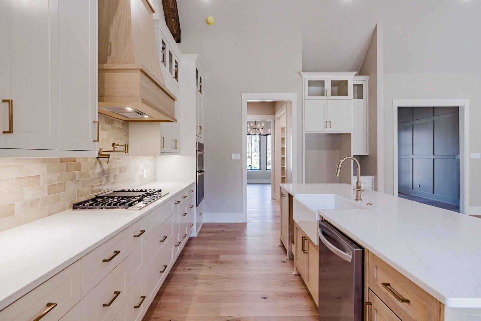 A kitchen with white upper cabinets, light wood lower cabinets, a white island with a farmhouse sink, and stone backsplash.