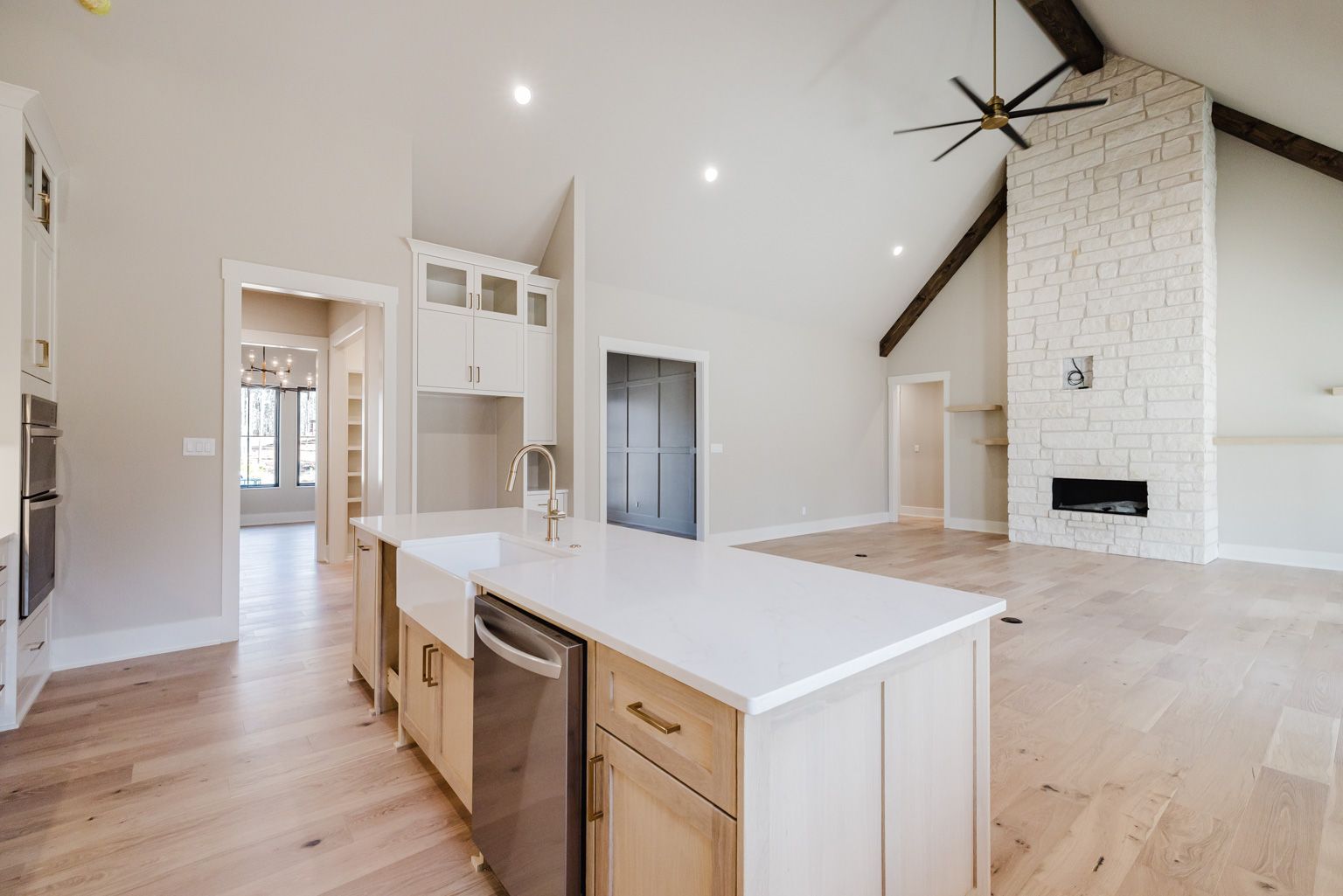 A kitchen island with a farmhouse sink and dishwasher, open to a living area with a white stone fireplace.