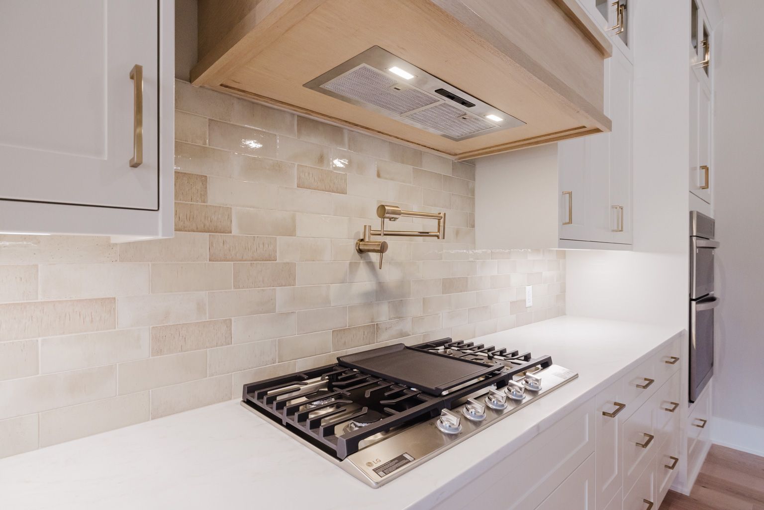 A modern kitchen features a stainless steel gas cooktop with a pot filler faucet against a light tiled backsplash.