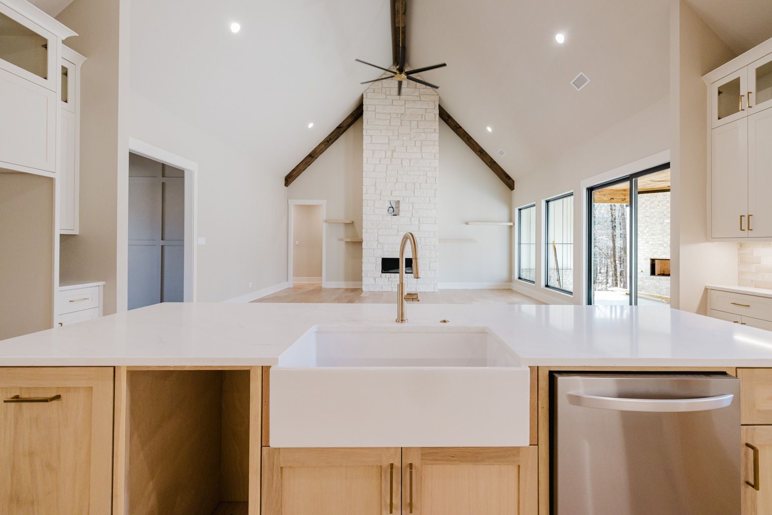 A kitchen island with a farmhouse sink faces a bright, open living room with a stone fireplace and vaulted ceiling.