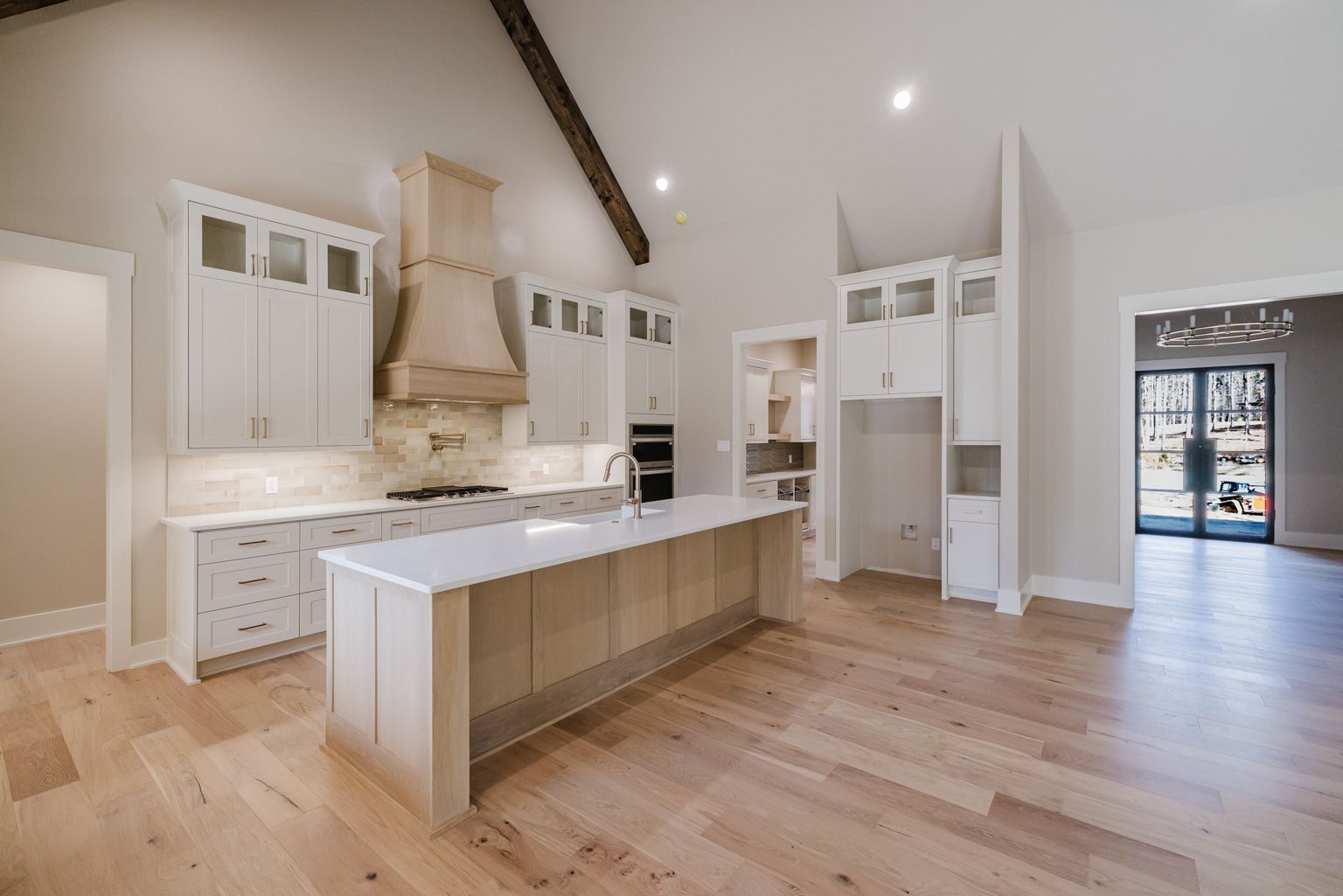 Modern kitchen with white cabinets, a large island, wood range hood, and light wood floors under a vaulted ceiling.