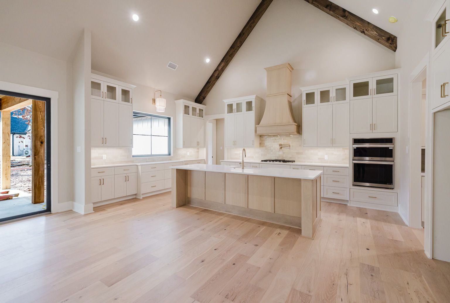 A bright, modern kitchen featuring white cabinets, a large central island, light wood floors, and a vaulted ceiling.