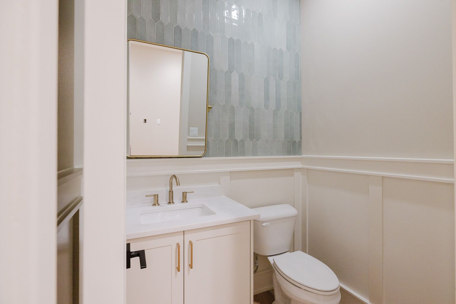 A small bathroom features a white vanity, a modern faucet, a mirror, a toilet, and a light blue vertical tile backsplash.