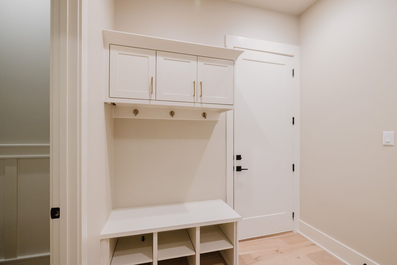A white mudroom entry with wall-mounted storage cabinets, coat hooks, and a bench with open cubbies.