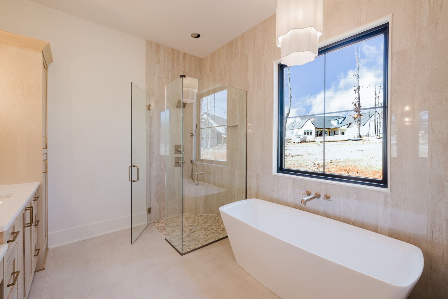 A modern bathroom featuring a white freestanding tub, a glass-enclosed shower, and a large window with a view.