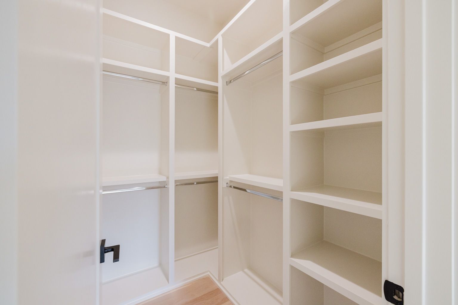 A walk-in closet with white walls, shelves, and hanging rods on both sides.