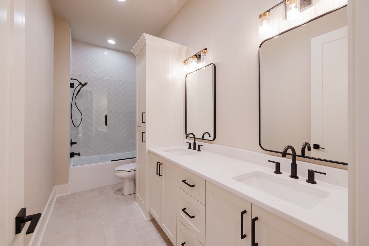 A modern bathroom with a double vanity, white cabinets, black hardware, two mirrors, and a tiled tub-shower combo.