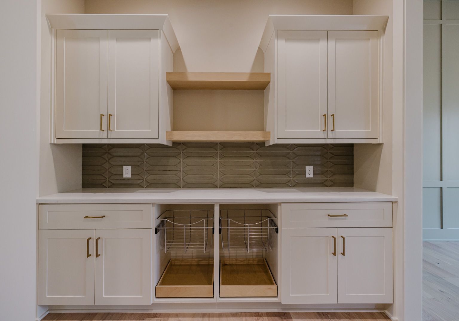 White kitchen cabinets with brass hardware, open wood shelves, and a gray textured backsplash over a prep station.