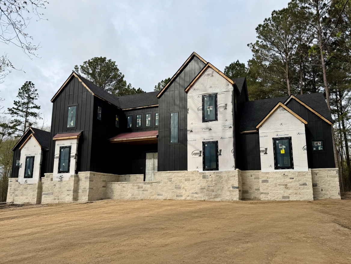 A two-story home under construction with black siding, light stone foundation, and multiple gabled roofs.