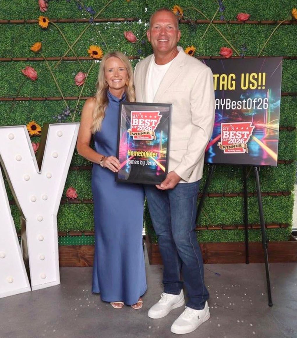 Two people holding award plaques in front of a green wall and sign at an event
