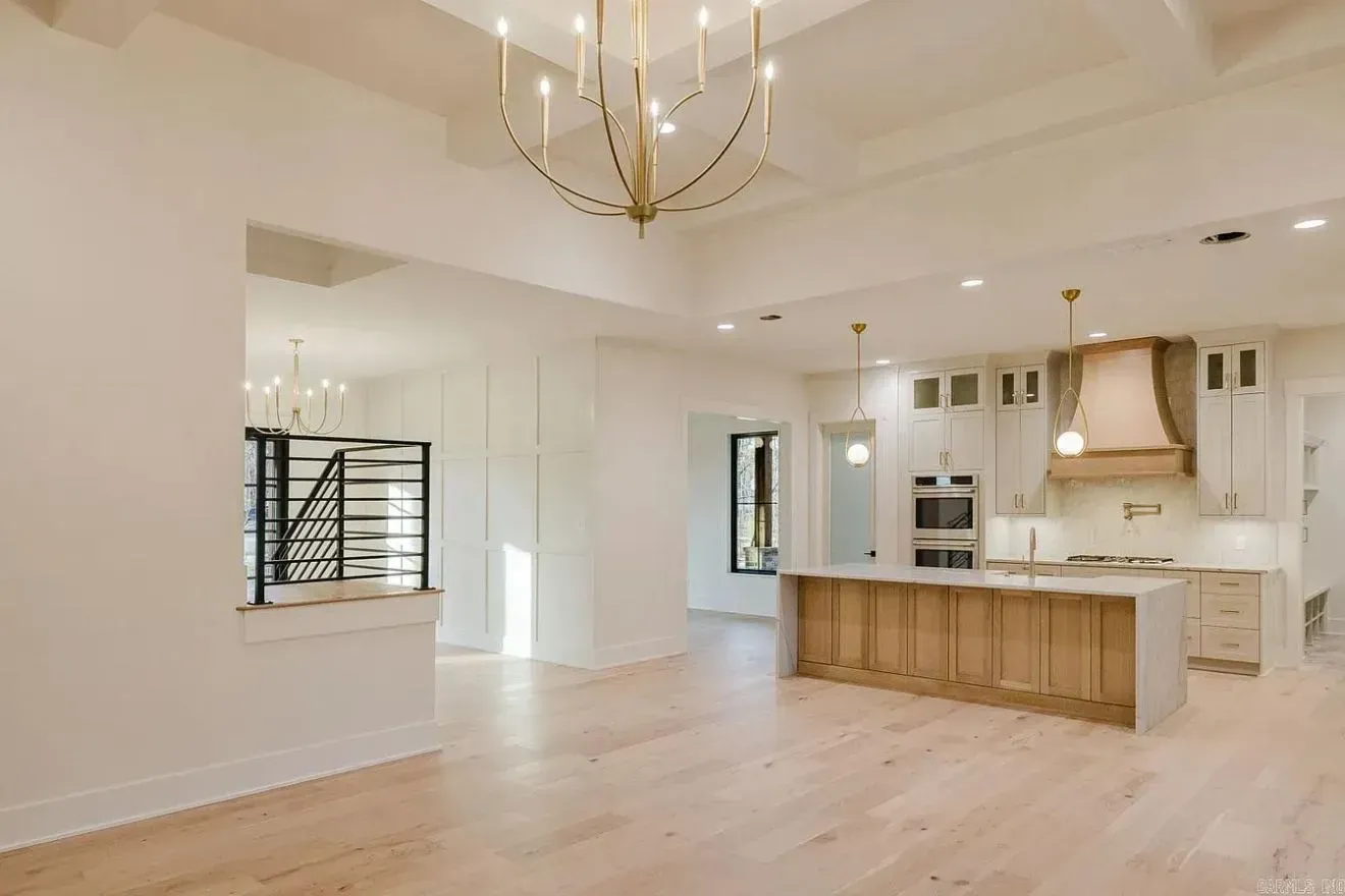 An open-concept living area with light wood floors, a gold chandelier, and a white kitchen with a wooden island.