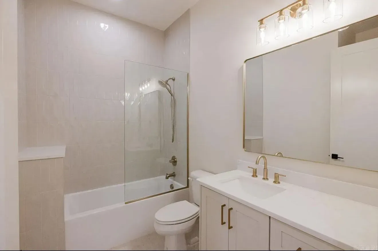 A modern bathroom featuring a white vanity, a large wall mirror, and a bathtub with a glass shower screen.