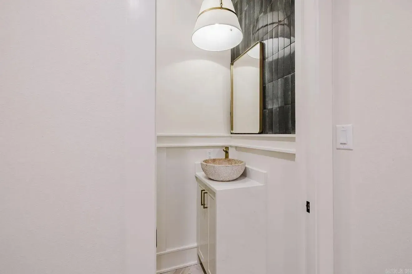 A small powder room with a white vanity, vessel sink, gold faucet, wall-mounted mirror, and a geometric pendant light.
