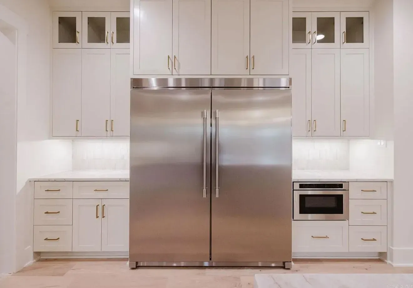 A stainless steel refrigerator sits between white kitchen cabinets and drawers, with an integrated microwave to the right.