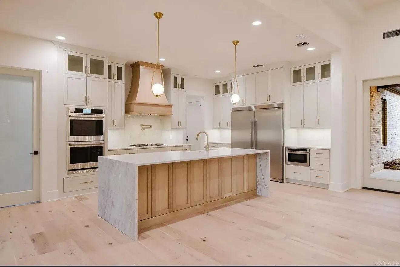 A modern kitchen with white cabinetry, a large marble-topped island with wood paneling, and stainless steel appliances.