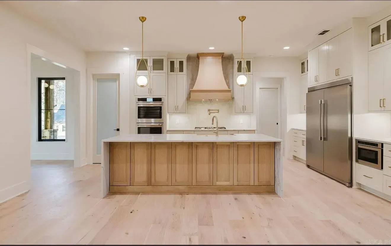 Modern kitchen with light wood island, white cabinets, stainless steel appliances, and dual pendant lights.