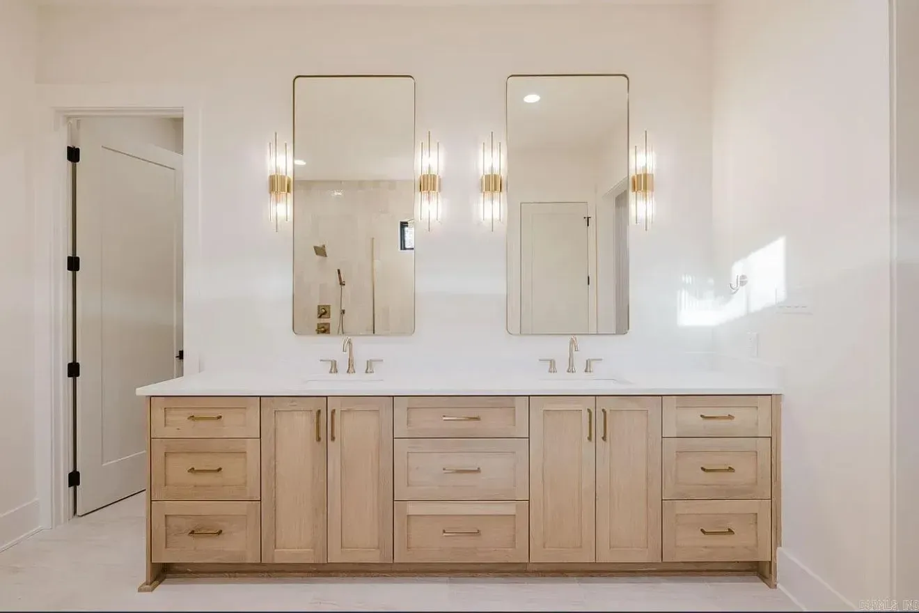 A bathroom vanity with light wood cabinets, double sinks, two rectangular mirrors, and brass light fixtures.