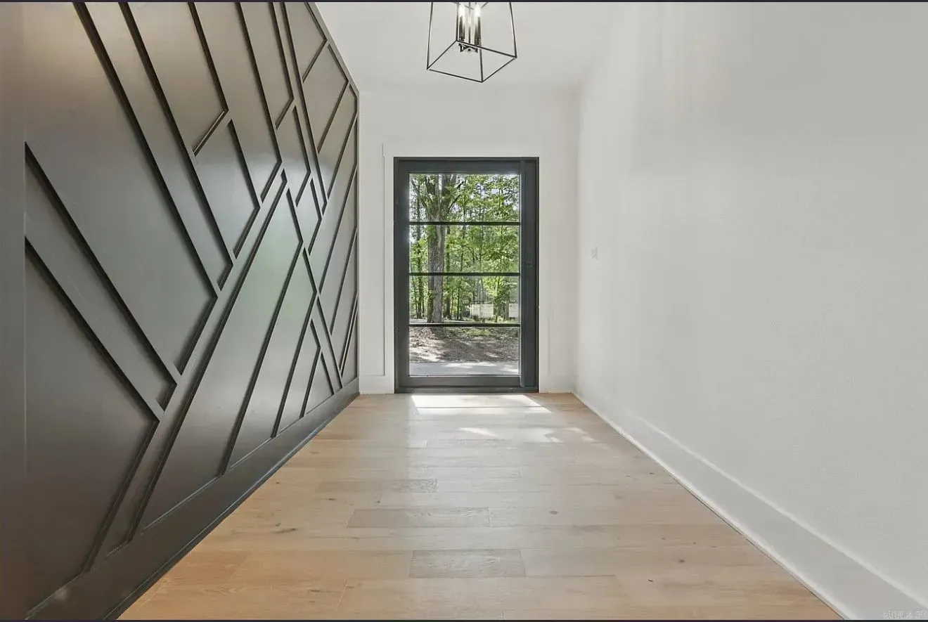 Modern entryway with light wood floors, white walls, and a geometric-patterned dark gray accent wall facing a glass door.