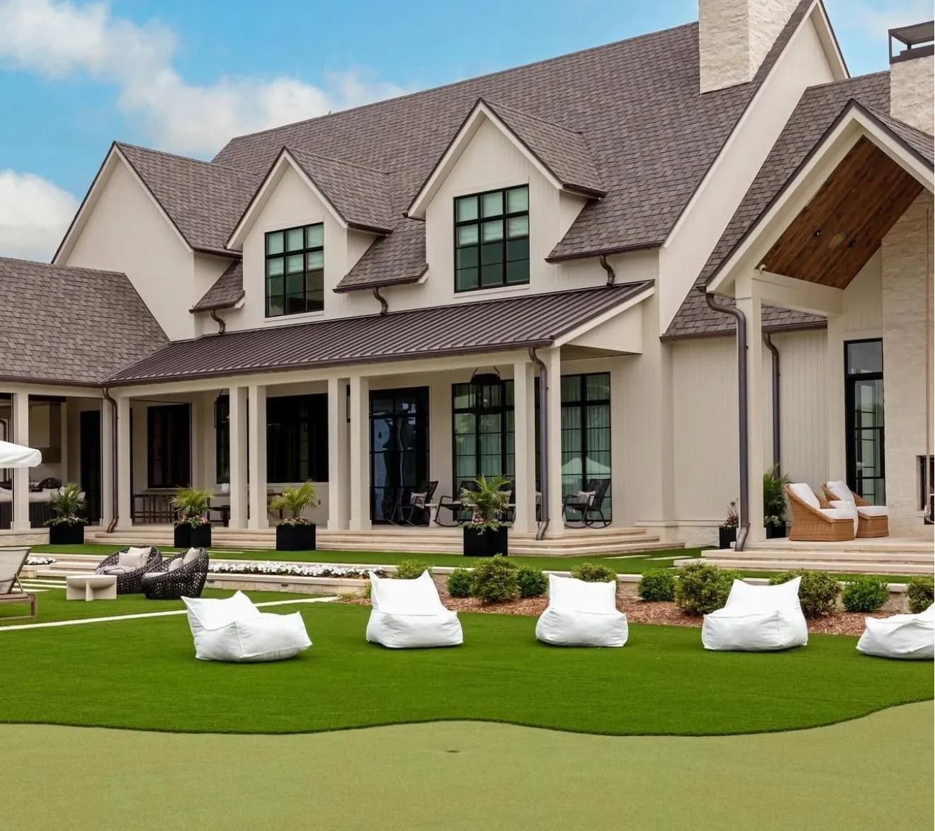 A large cream-colored house with a dark shingled roof, a covered porch, and white bean bag chairs on a green lawn.