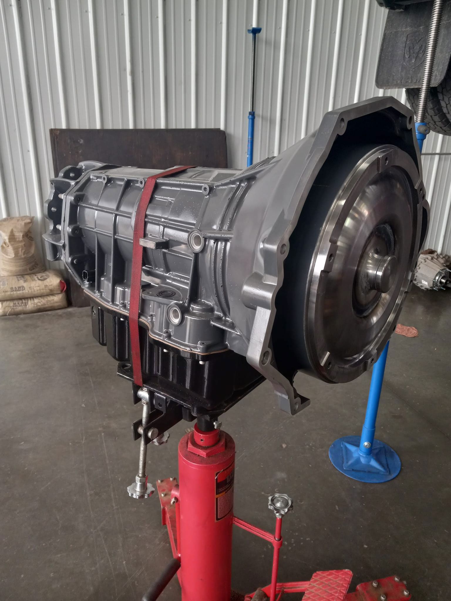 A gearbox is sitting on top of a red jack in a garage.