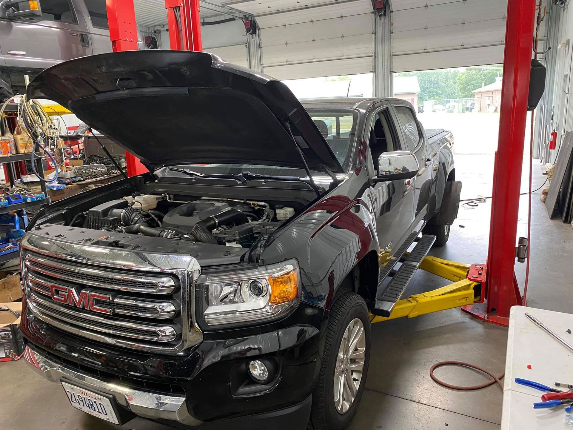A gmc truck with its hood up is on a lift in a garage.
