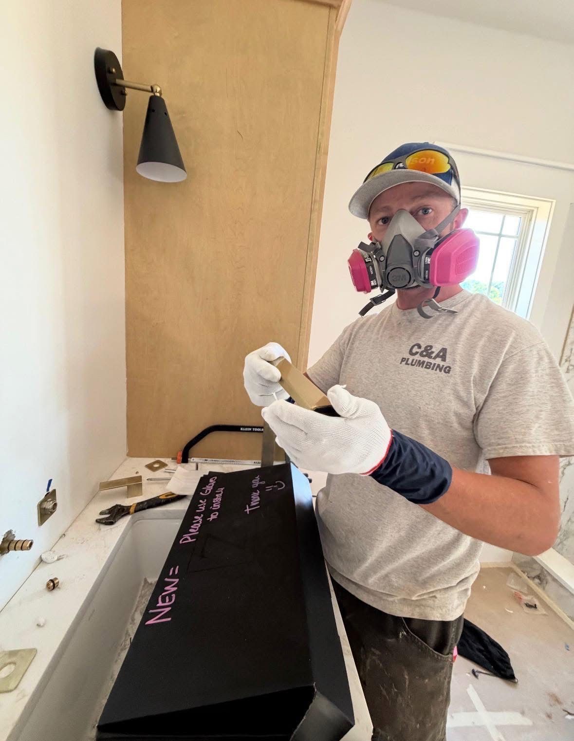 Person in respirator and gloves holds a black box in a room under renovation.