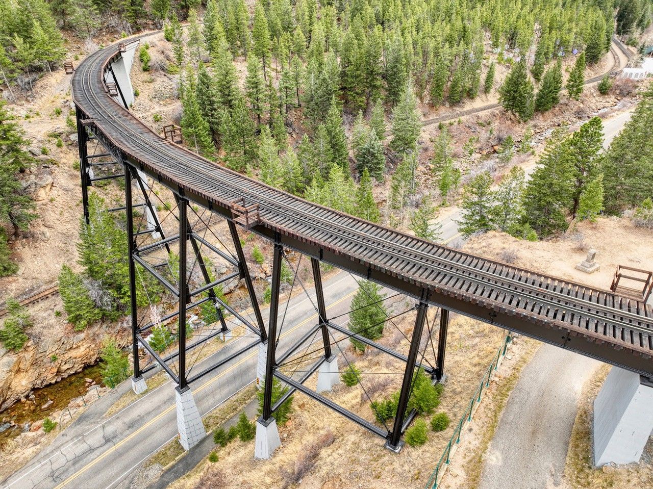 A curved trestle bridge over a forested valley, with black supports and a road below.