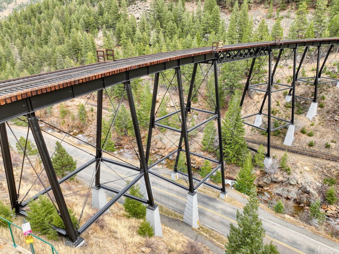 Elevated wooden trestle bridge with black steel supports over a rocky forested slope.