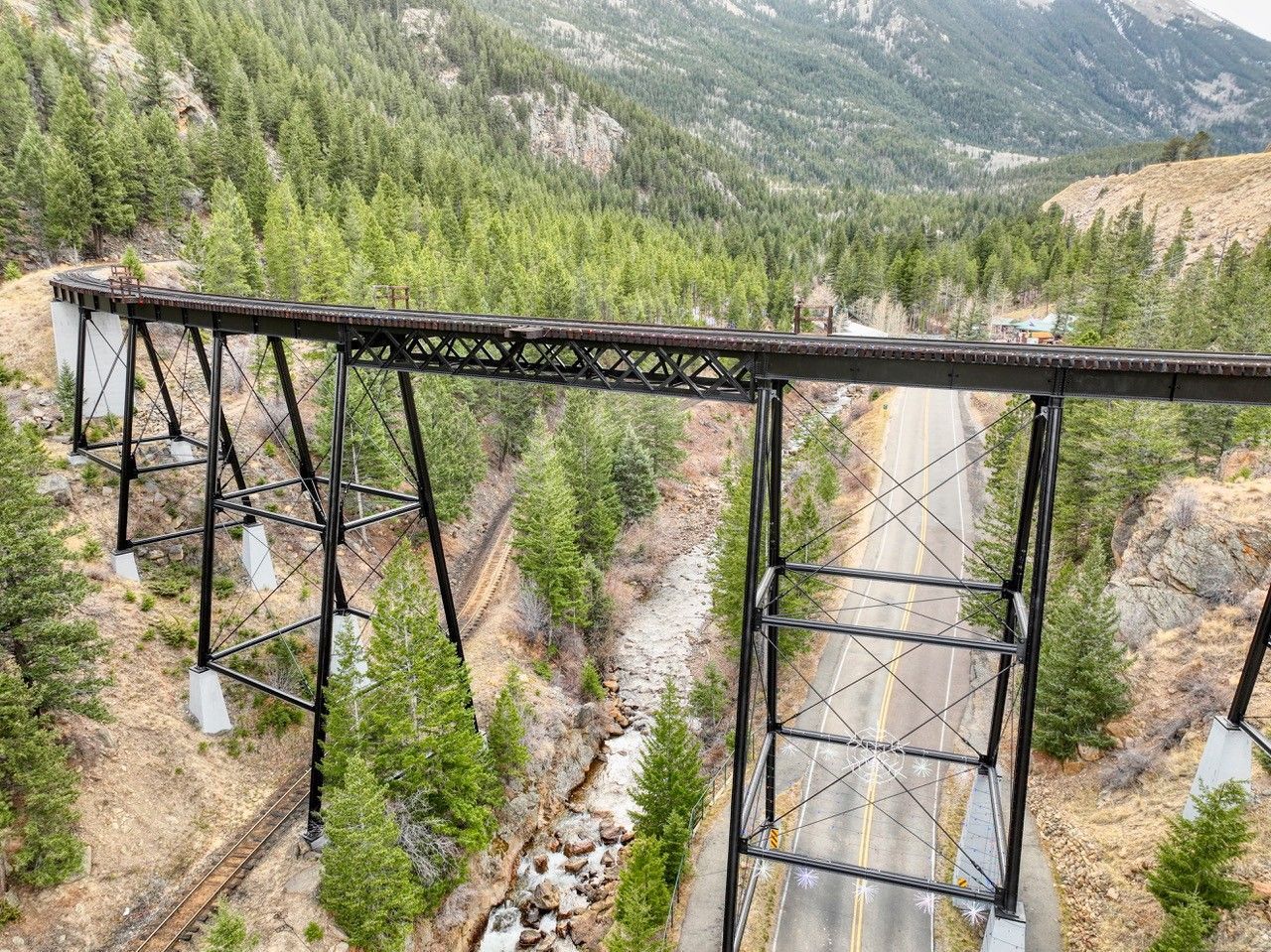 Abandoned steel trestle bridge spanning a rocky mountain ravine with pine trees below.